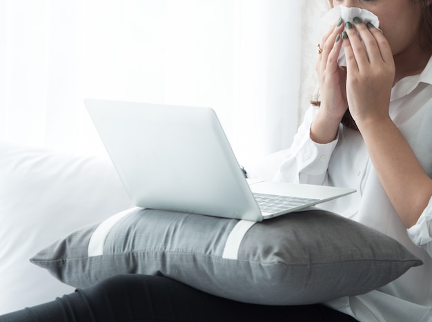 Cuando una mujer tiene fiebre, estornuda cuando usa una computadora portátil en el dormitorio.