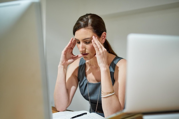 Cuando el trabajo se vuelve demasiado difícil de manejar Fotografía de una mujer de negocios que sufre dolor de cabeza en el escritorio de su oficina