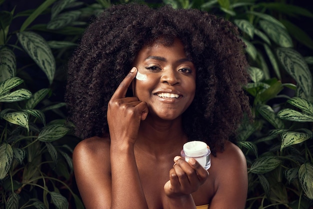 Cuantos menos productos químicos, más feliz mi piel Foto de una hermosa joven que se aplica crema hidratante en la cara contra un fondo frondoso