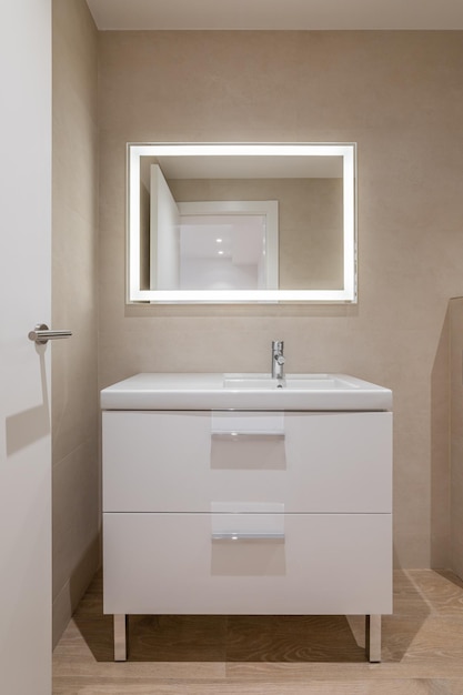 Cuarto de baño moderno con muebles de azulejos beige y espejo grande rectangular con iluminación
