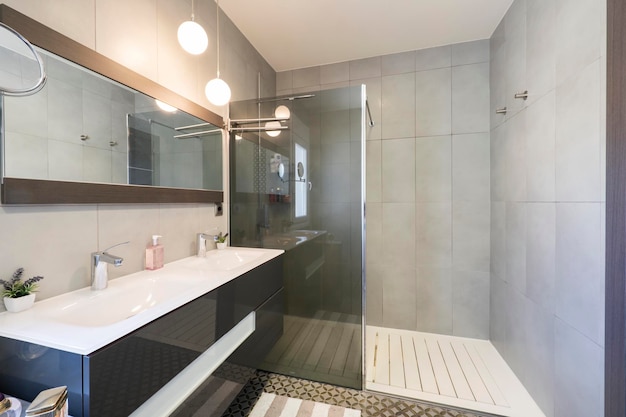 Cuarto de baño con mueble gris espejo rectangular con lavabo doble blanco y cabina de ducha con mampara de cristal gris