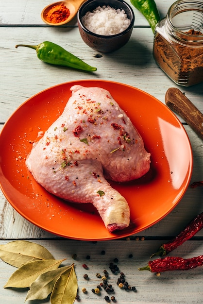 Cuarto de pierna de pollo en placa naranja sobre superficie de madera con diferentes especias