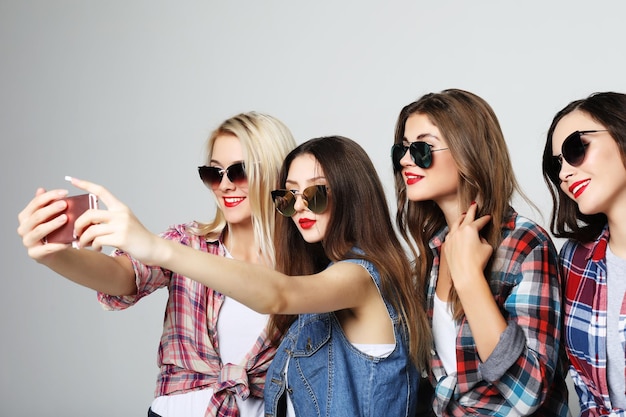 Cuatro adolescentes felices con smartphone tomando selfie