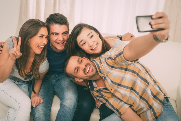 Foto cuatro alegres mejores amigos pasando un buen rato en un apartamento y tomándose selfie.