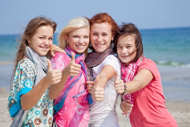 Cuatro amigas abrazadas en la playa muestran el símbolo OK.