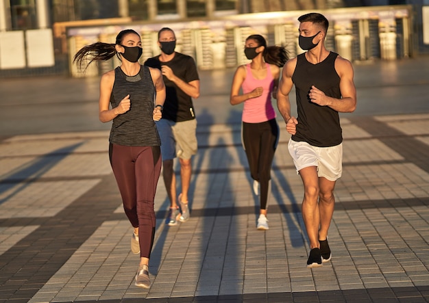 Cuatro amigos en máscaras protectoras haciendo deporte juntos.