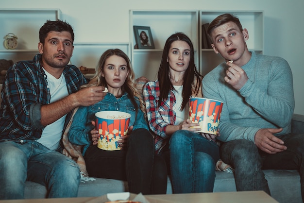 Los cuatro amigos con palomitas de maíz miran una película de terror en el sofá