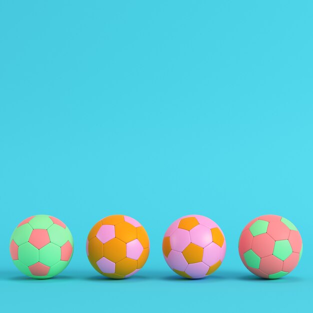 Foto cuatro balones de fútbol de colores sobre fondo azul brillante