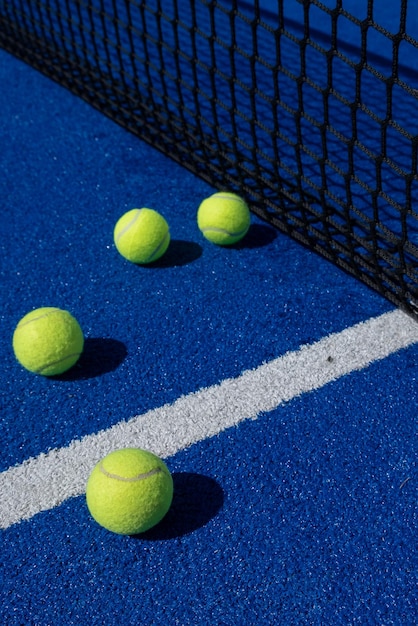 cuatro bolas al lado de la red y la línea central de una cancha de tenis de paleta azul