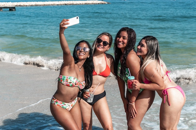 Cuatro chicas guapas disfrutando de un día de playa, tomándose fotos.