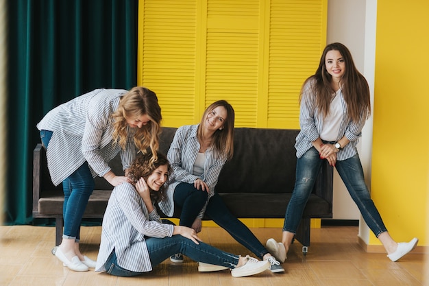 Cuatro chicas jóvenes con camisas de rayas, jeans y zapatillas posando en el sofá. estudio de rodaje.