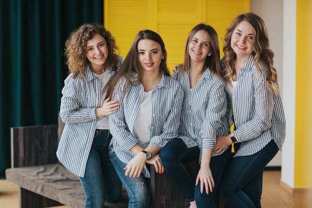 Foto cuatro chicas jóvenes con camisas de rayas, jeans y zapatillas posando en el sofá. estudio de rodaje.