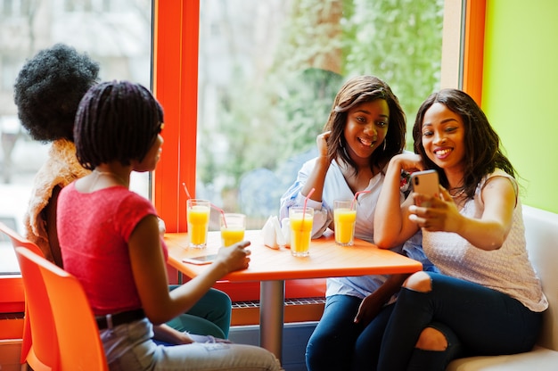 Cuatro chicas jóvenes con jugos sentados y haciendo selfie por teléfono