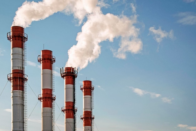 Cuatro chimeneas de fábrica humeantes en el cielo azul