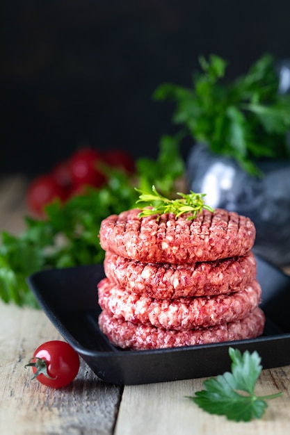 Cuatro chuletas de hamburguesa cruda con carne picada con sal, hierbas y especias en una sartén a la parrilla