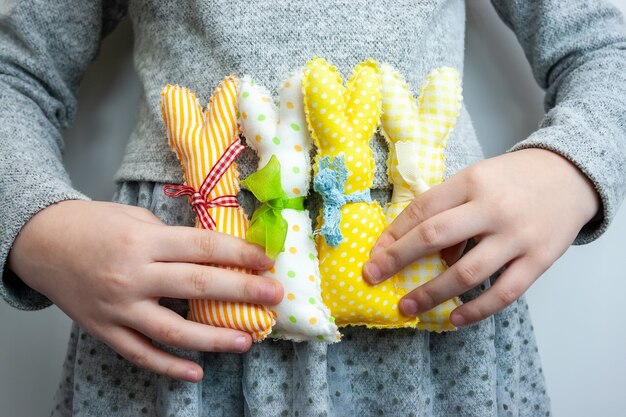 Cuatro coloridos conejitos de Pascua hechos a mano brillantes en manos de una niña vestida de gris