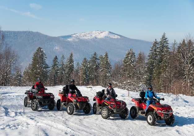 Cuatro conductores de ATV en quads todoterreno en la cima de la montaña en invierno