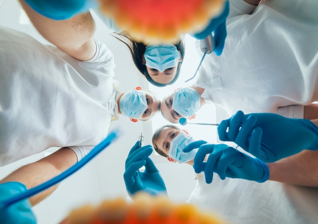 Cuatro dentistas uniformados realizan la operación de implantación dental en un paciente en la oficina de odontología