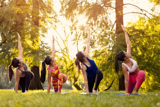 Foto cuatro hermosas amigas haciendo yoga en el parque.