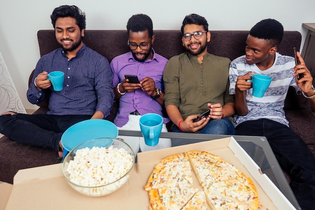 cuatro hombres afroamericanos comiendo pizza en la fiesta de casa, tirándose palomitas de maíz entre ellos.