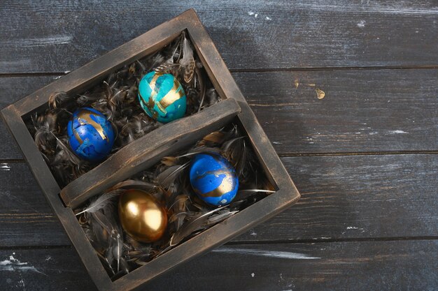 Cuatro huevos de Pascua de colores pintados sobre piel de animal en caja de madera oscura sobre fondo de madera oscura Estilo boho