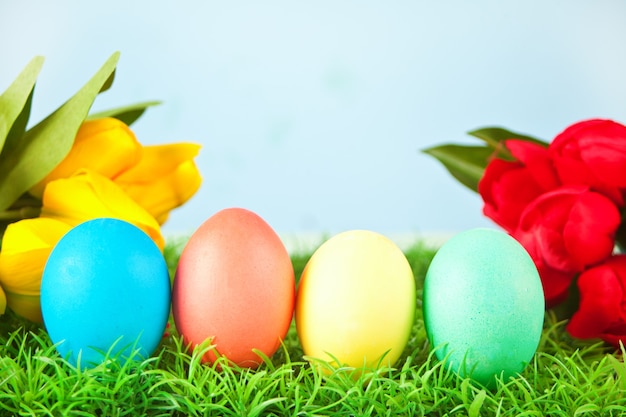 Cuatro huevos de Pascua decorados en la hierba con tulipanes de flores en el fondo.