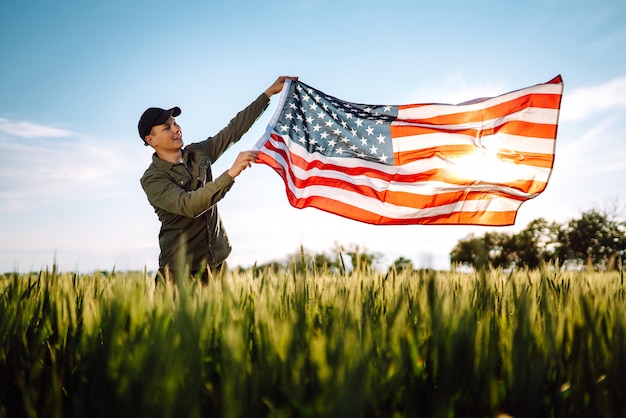 Cuatro de Julio. Hombre patriótico con la bandera nacional estadounidense en el campo. Joven con orgullo ondeando una bandera estadounidense. Día de la Independencia.