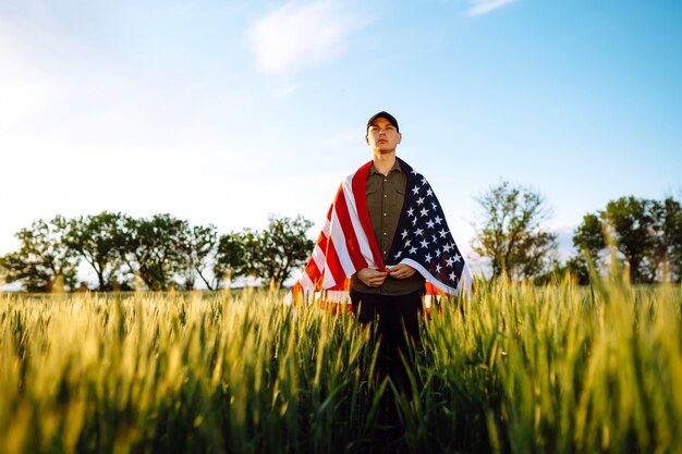 Cuatro de Julio. Hombre patriótico con la bandera nacional estadounidense en el campo. Joven con orgullo ondeando una bandera estadounidense. Día de la Independencia.