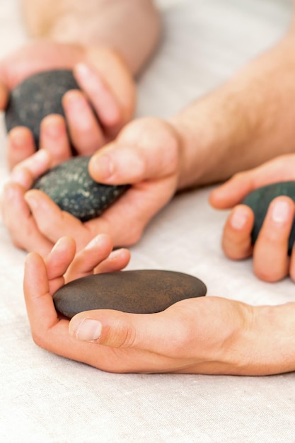 Cuatro manos de masajistas masculinos sosteniendo piedras de spa en la vista superior de la toalla blanca. Concepto de masaje con piedras.