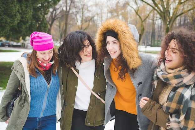 Cuatro mujeres jóvenes multiétnicas abrazando nieve campo riendo