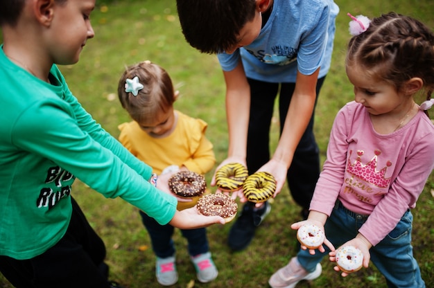 Foto cuatro niños con donas en el patio de la tarde. comida deliciosa deliciosa rosquilla.