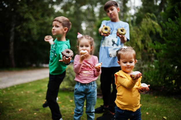 Cuatro niños con donas en el patio de la tarde. Comida deliciosa deliciosa rosquilla.