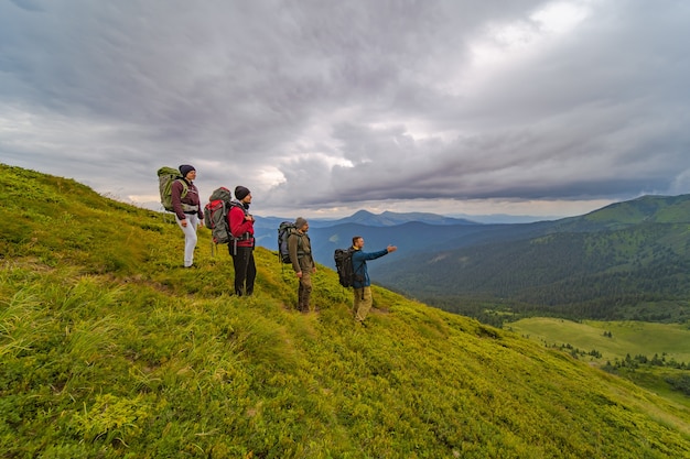 Las cuatro personas activas con mochilas de pie en la montaña verde.