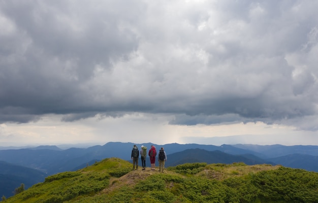 Las cuatro personas activas de pie en la montaña contra hermosas nubes.