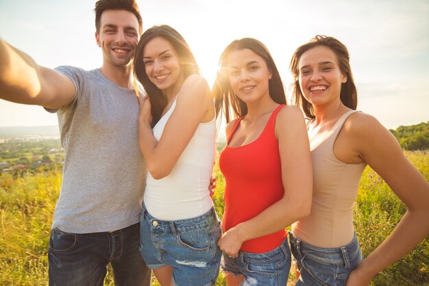 Las cuatro personas felices hacen un selfie en el fondo del sol brillante