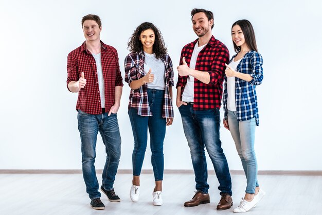 Las cuatro personas felices pulgar hacia arriba en el fondo de la pared blanca