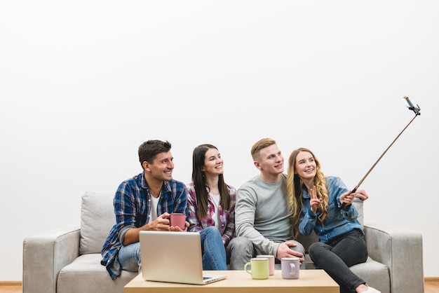 Las cuatro personas hacen un selfie en el sofá en el fondo de la pared blanca