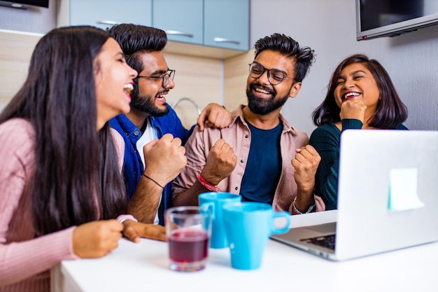 Cuatro personas indias en la cocina mirando la computadora portátil y discutiendo una tarea de aprendizaje a distancia