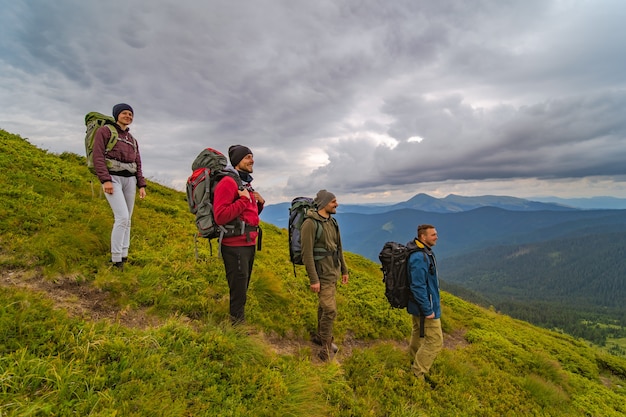 Las cuatro personas con mochilas de pie en la montaña verde.