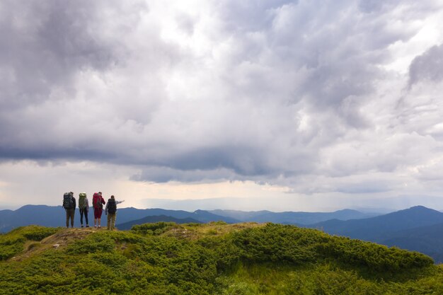 Las cuatro personas con mochilas de pie sobre una montaña contra hermosas nubes