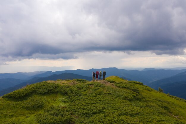 Las cuatro personas con mochilas de pie sobre una montaña contra hermosas nubes