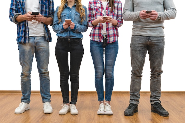 Foto las cuatro personas con teléfonos están parados en el fondo de la pared blanca