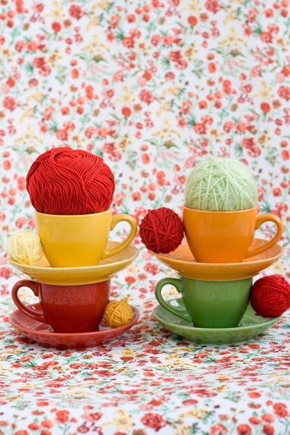 Cuatro tazas de colores y bolas de hilo sobre un fondo de una flor roja