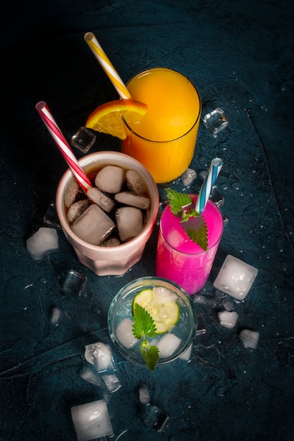 Foto cuatro tipos de bebidas refrescantes con hielo sobre una superficie azul oscura y cubitos de hielo.