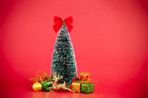 Foto cubierta del árbol de pino de navidad con nieve decorando con adornos de navidad sobre fondo rojo