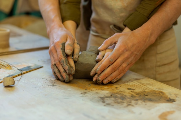 Cubierto de arcilla. Encantadora pareja romántica que tiene una clase magistral en el taller de cerámica mientras sostiene suavemente la arcilla juntos