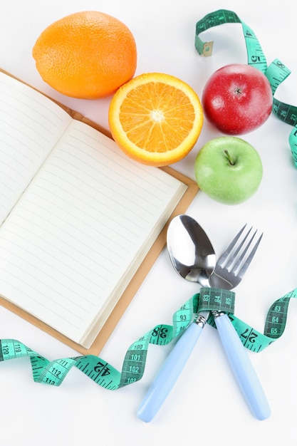 Cubiertos atados con cinta métrica y libro con fruta aislado en blanco