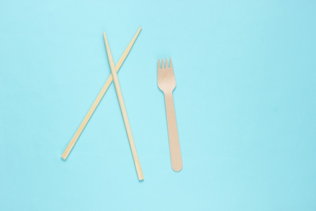 Cubiertos ecológicos. Palillos chinos, tenedor de madera sobre fondo azul.