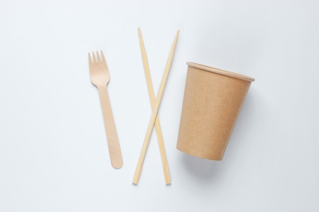 Cubiertos ecológicos. Palillos chinos, tenedor de madera, vaso de papel artesanal sobre fondo blanco. Concepto de eco minimalismo.