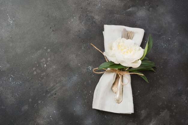 Cubiertos de elegancia con peonía blanca sobre mesa negra.